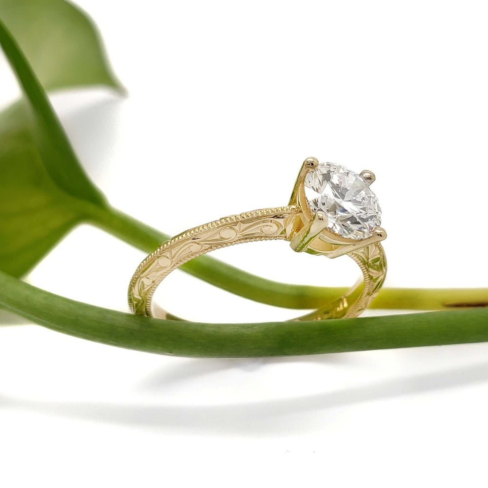 Hand-engraved 14kt yellow gold ring with round lab diamond, shown with green leaf