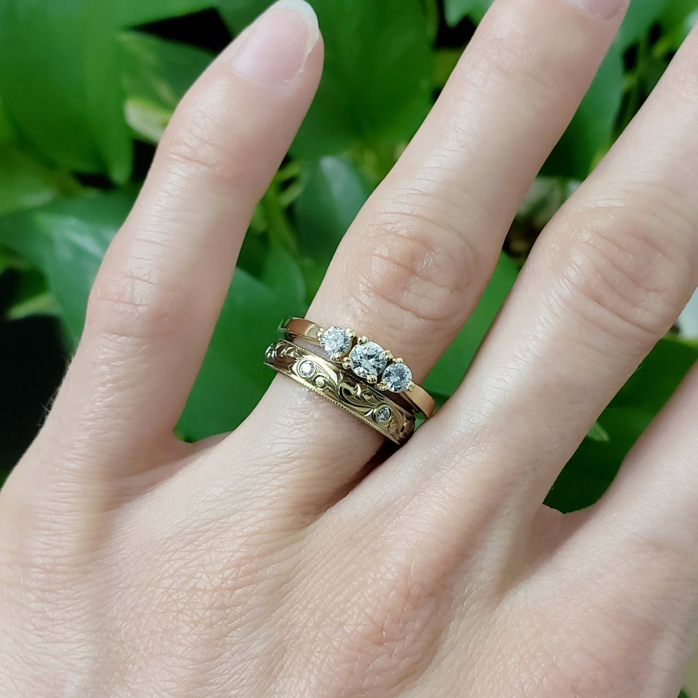 Hand-engraved yellow gold wedding band stacked with three-stone diamond ring on hand