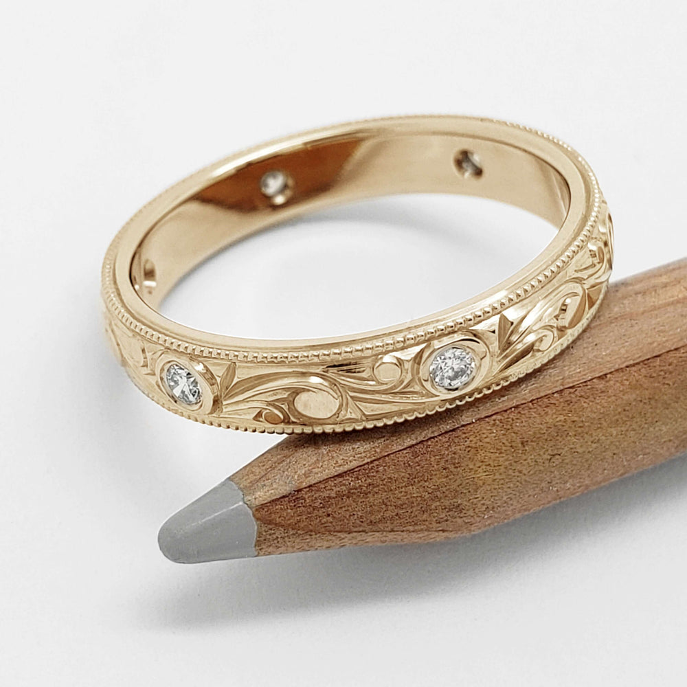 Hand-engraved yellow gold wedding ring with flush-set diamonds resting on pencil