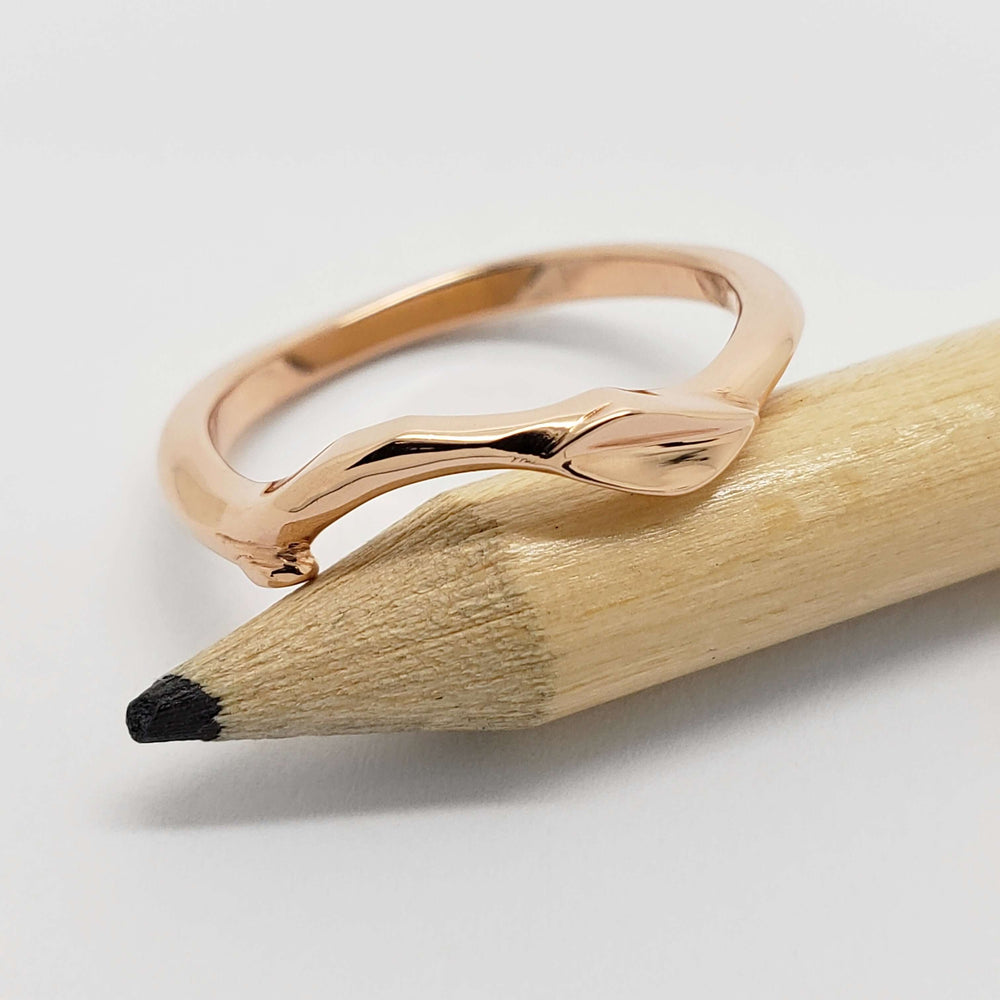 Hand carved 14kt rose gold leaf and twig ring displayed on a pencil