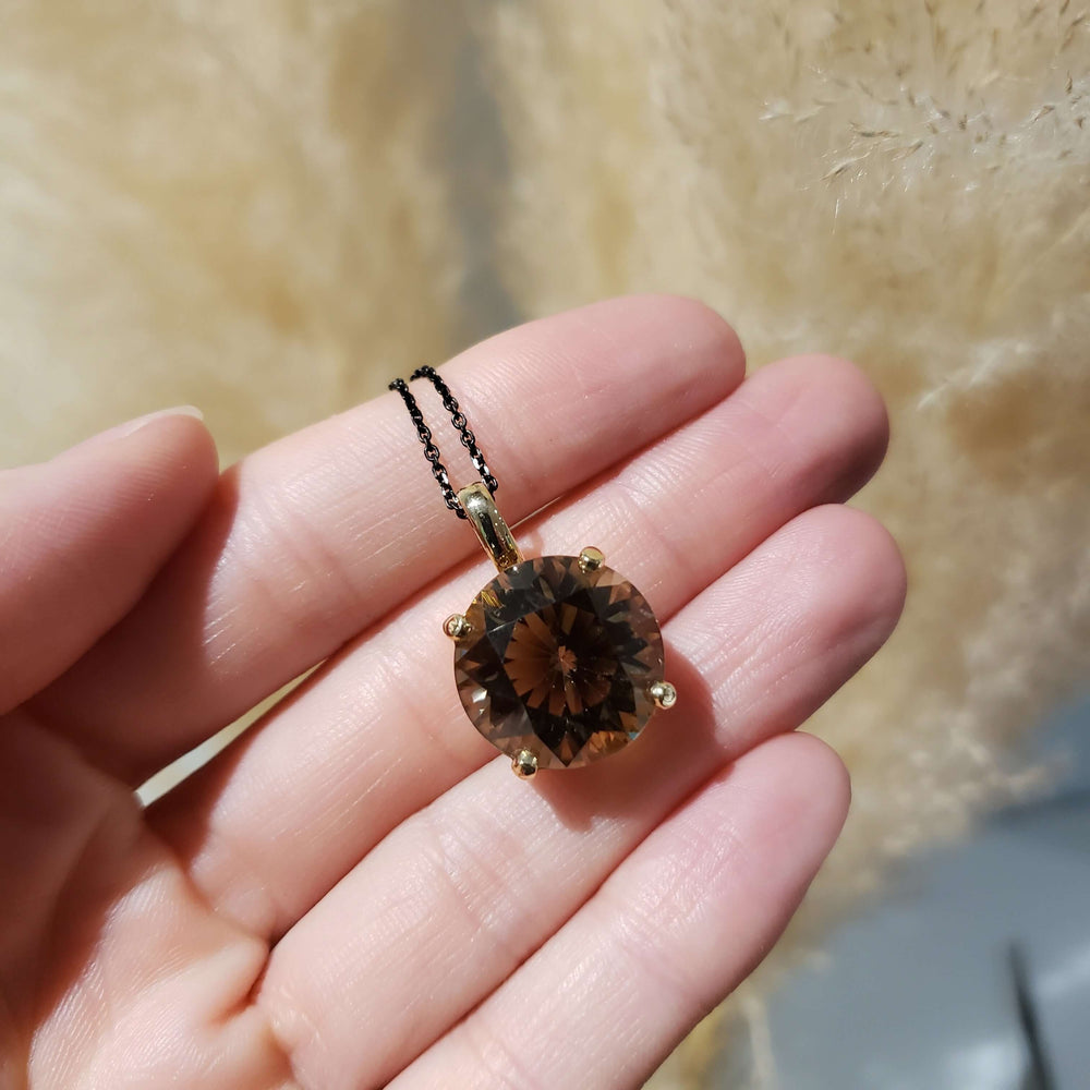 Hand holding 14kt yellow gold pendant with round smoky quartz on black chain