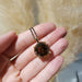 Hand holding 14kt yellow gold pendant with round smoky quartz on black chain