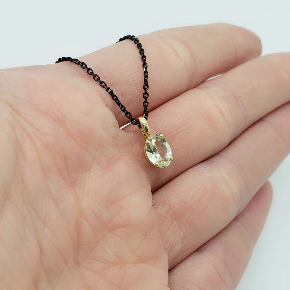 Hand holding an oval green beryl pendant in 14kt yellow gold on a black chain