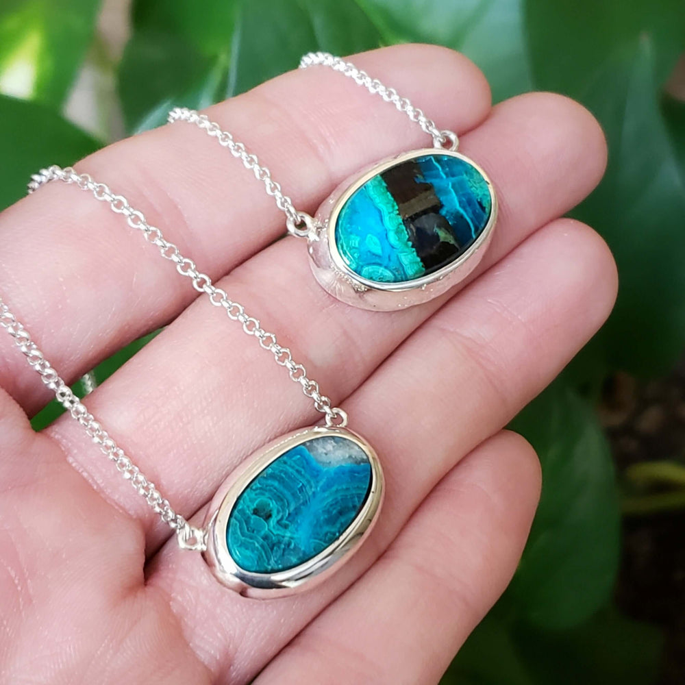 Hand holding two sterling silver necklaces with oval green-blue malachite pendants