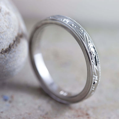 Hand engraved 14k white gold wedding ring with millgrain, shown beside a stone