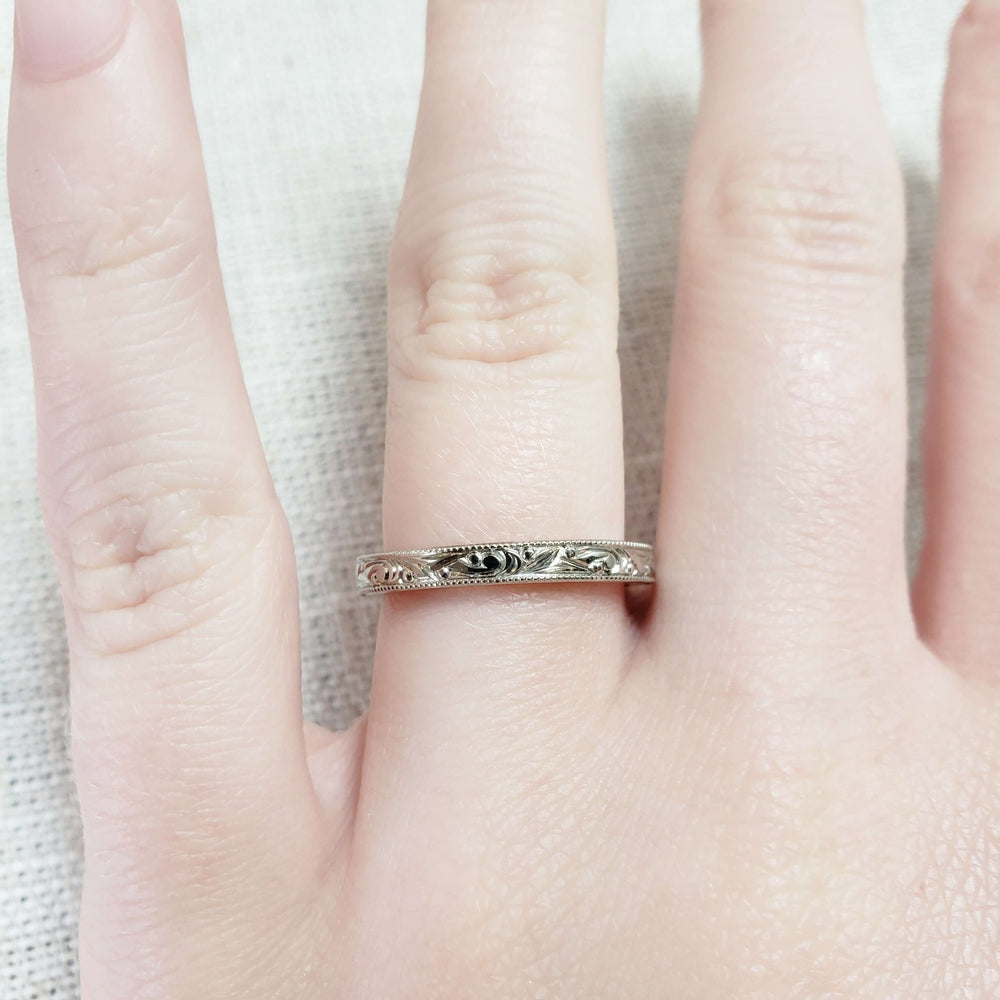 Hand engraved 14k white gold wedding ring with millgrain, worn on a finger