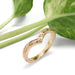 Hand engraved 14k yellow gold chevron wedding ring beside green leaves
