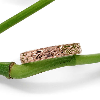 Hand engraved 14kt rose gold floral wedding ring resting on a green stem