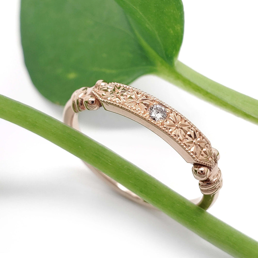 Hand engraved 14kt rose gold wedding ring with lab diamond, shown with green leaves