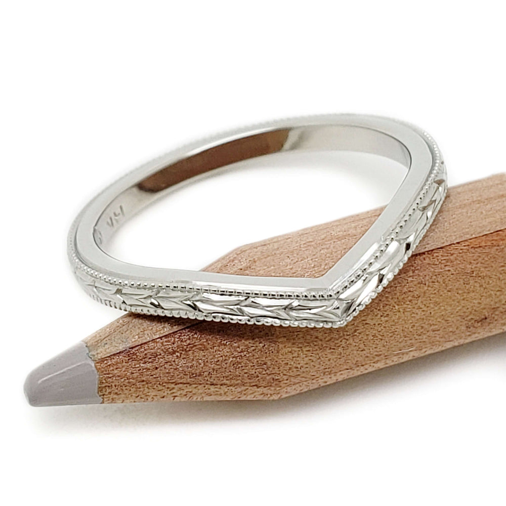Hand engraved 14kt white gold chevron ring resting on a pencil, wheat pattern visible