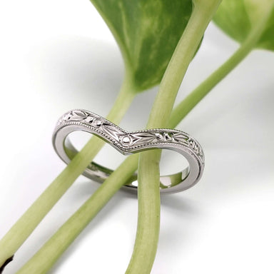 Hand engraved 14kt white gold chevron wedding ring displayed on green plant stems