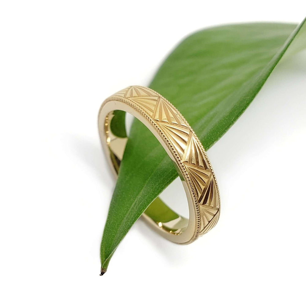 Hand engraved 14kt yellow gold Deco wedding ring displayed on a green leaf