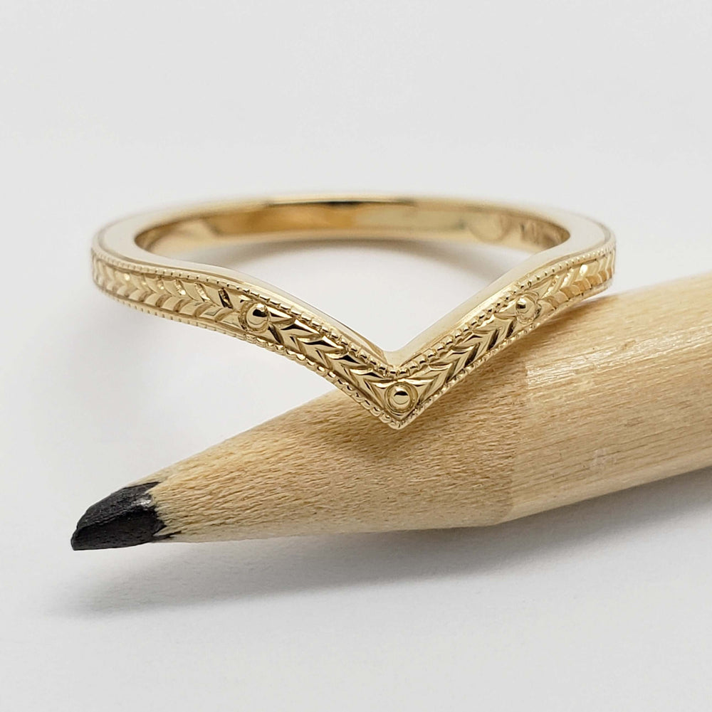 Hand engraved 14kt yellow gold chevron ring resting on a pencil