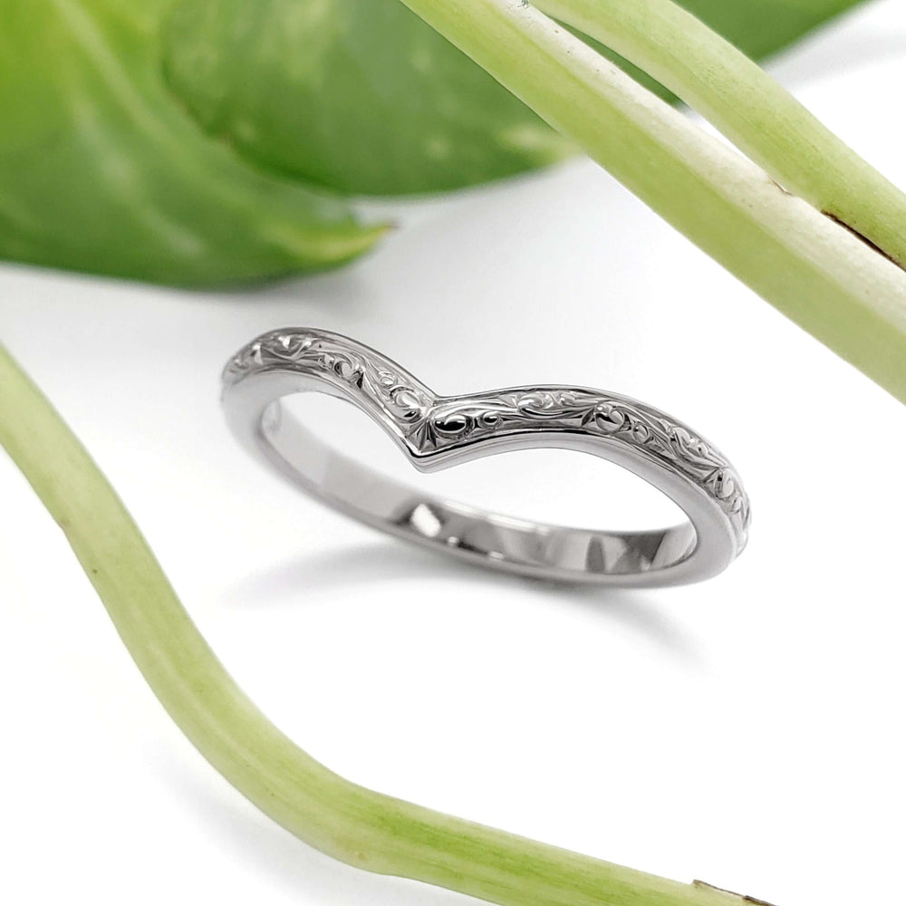 Hand engraved 14kt white gold chevron wedding ring beside green leaves