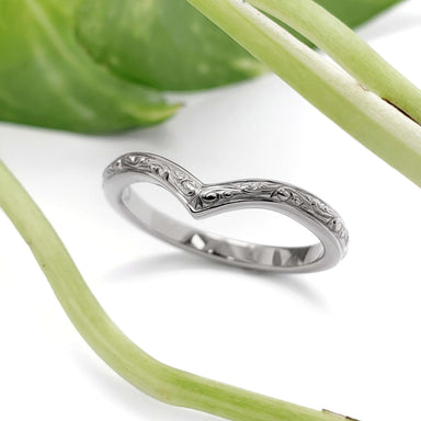 Hand engraved 14kt white gold chevron wedding ring beside green leaves