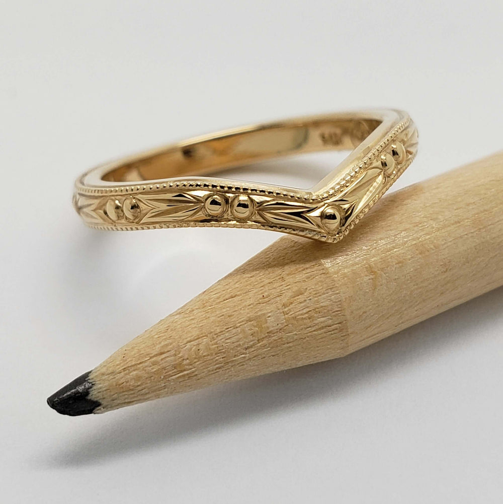 Hand engraved yellow gold chevron wedding ring with berry pattern beside a pencil