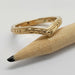 Hand engraved yellow gold chevron wedding ring with berry pattern beside a pencil