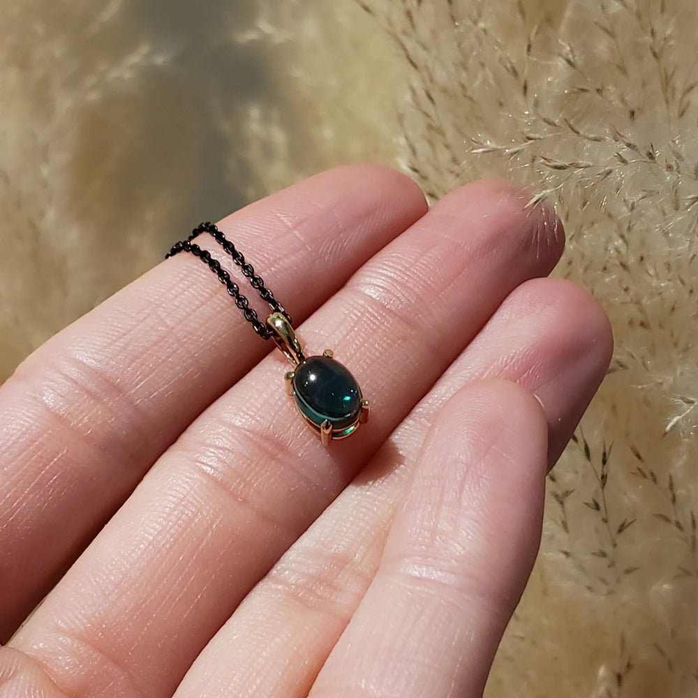 Hand holding a 14kt yellow gold pendant with oval cabochon lab emerald on black chain