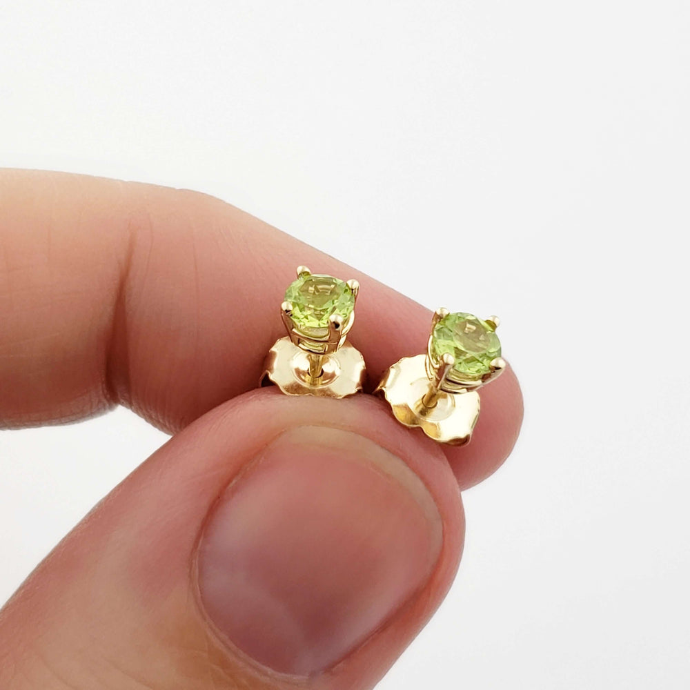 Hand holding 14kt yellow gold peridot stud earrings in a 4-claw setting