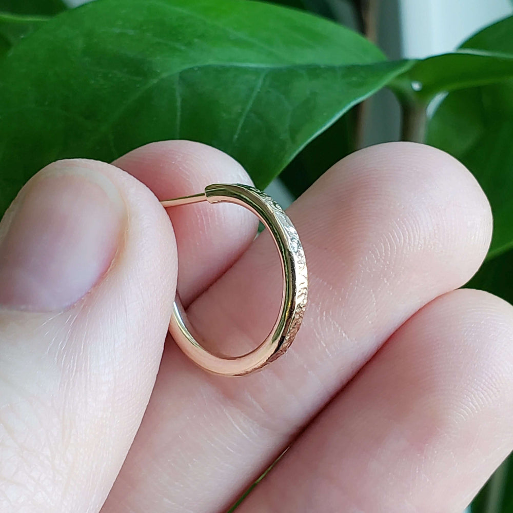 Close-up of a hand holding a 14kt yellow gold textured hoop earring