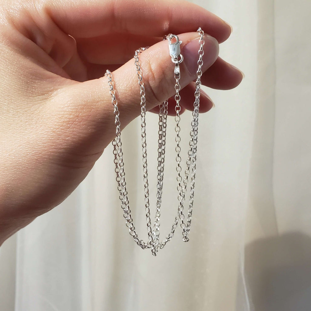 Hand holding a sterling silver cable chain necklace in natural light