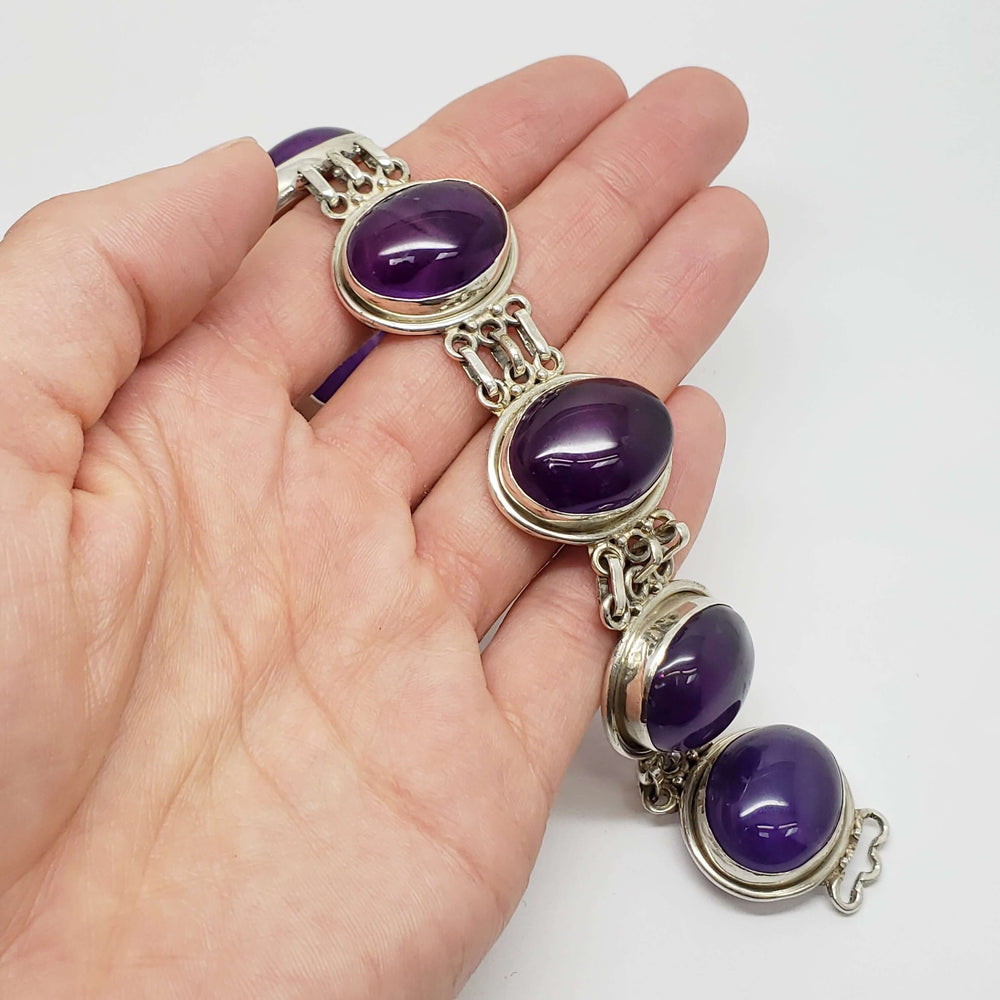 Hand holding vintage sterling silver bracelet with large amethyst cabochons