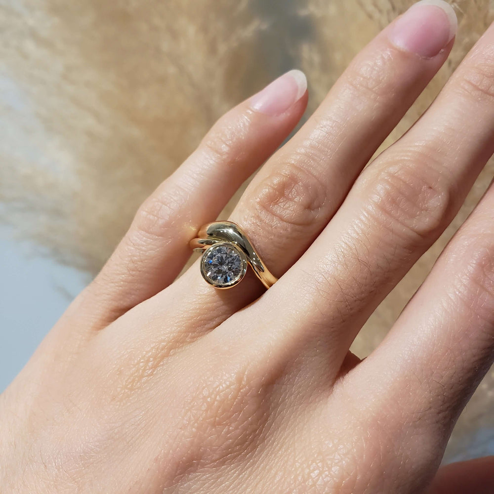 Hand wearing 14kt yellow gold curvy engagement ring with bezel-set lab diamond