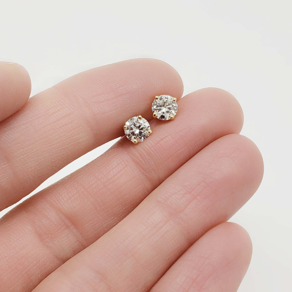Hand holding a pair of round brilliant lab diamond stud earrings in 14kt yellow gold