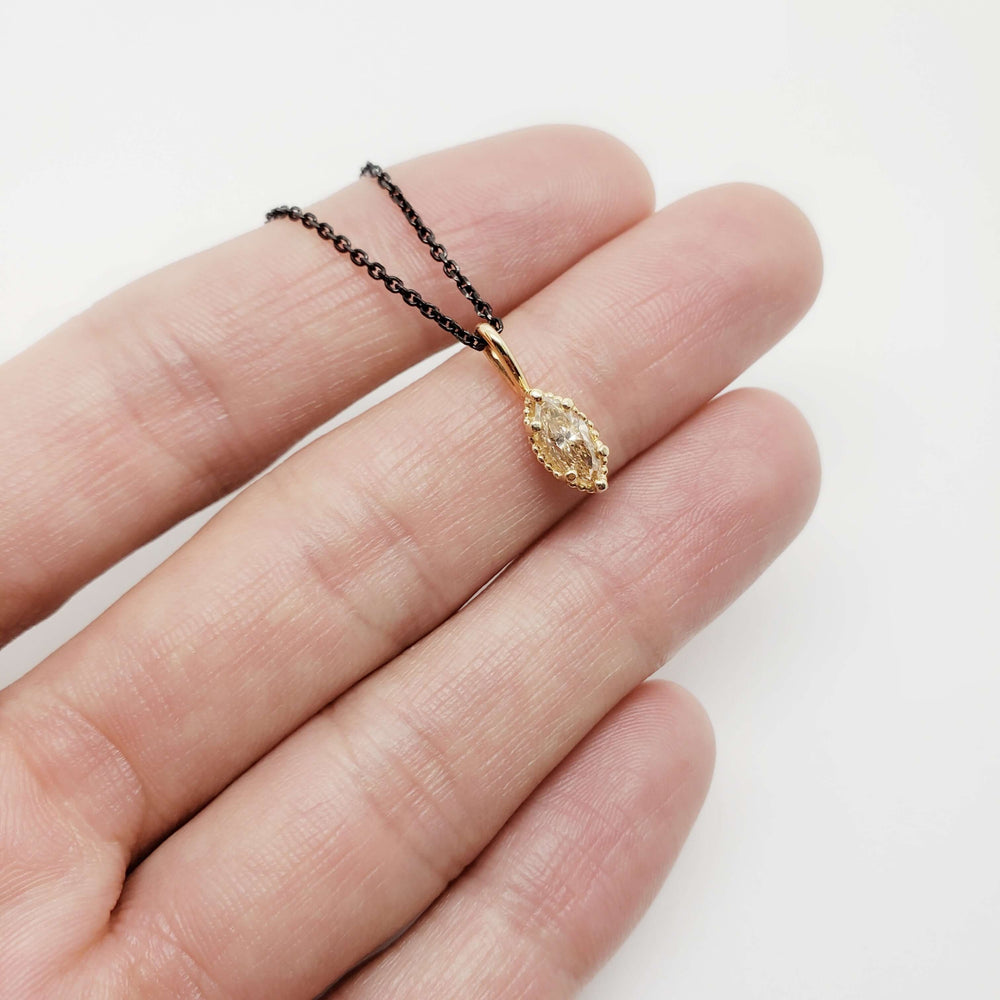 Hand holding a marquise champagne diamond pendant in 14kt yellow gold on a black chain