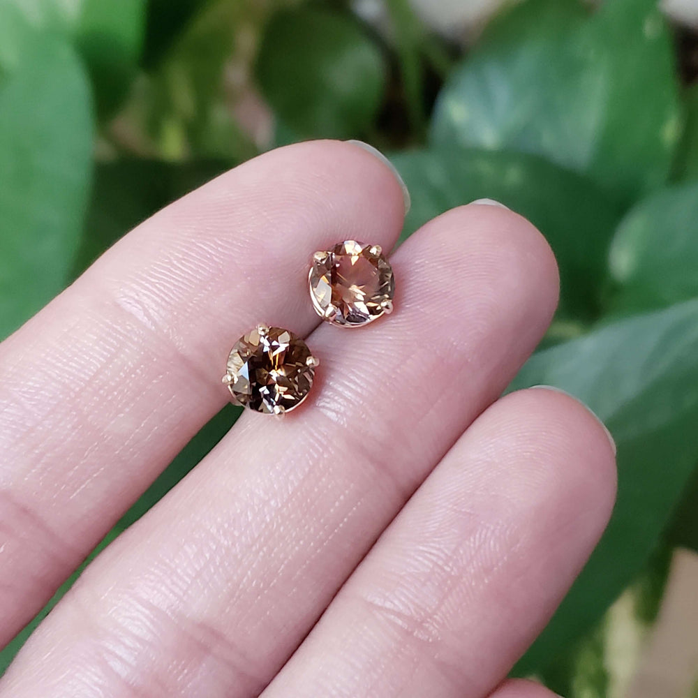 Hand holding round smoky quartz stud earrings in yellow gold