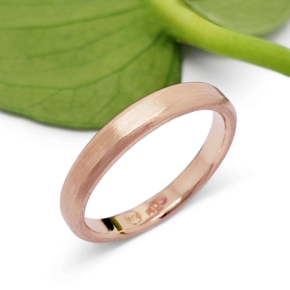 Handcrafted 14k rose gold wedding ring with brushed texture beside a green leaf
