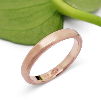 Handcrafted 14k rose gold wedding ring with brushed texture beside a green leaf