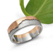 Handcrafted 14k white and rose gold mountain range ring beside a green leaf