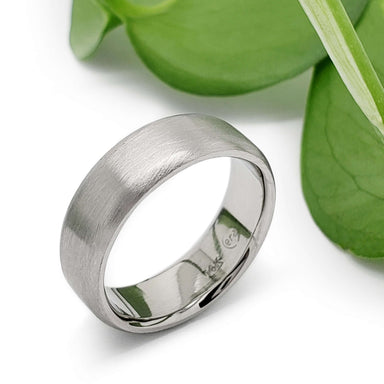 Handcrafted 14k white gold flat wedding ring beside green leaves