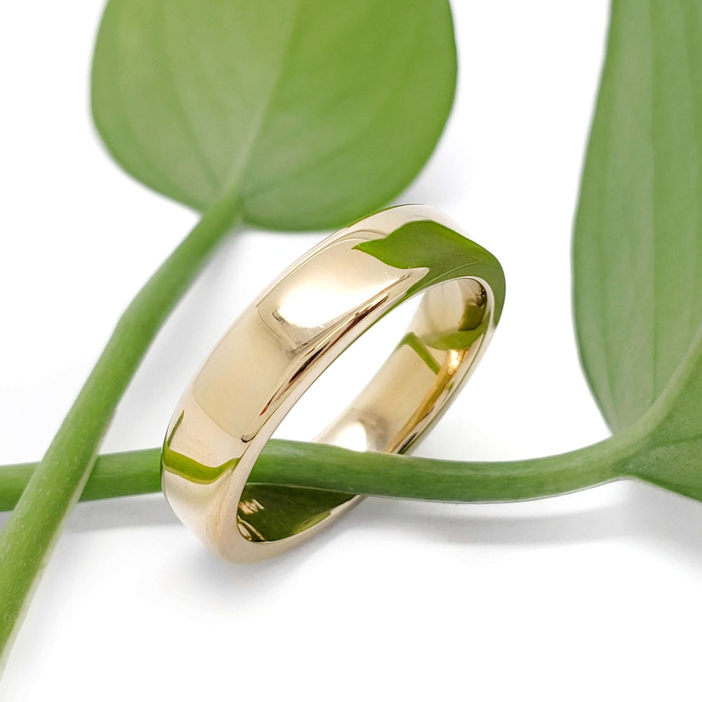Handcrafted 14k yellow gold wedding band displayed with green leaves