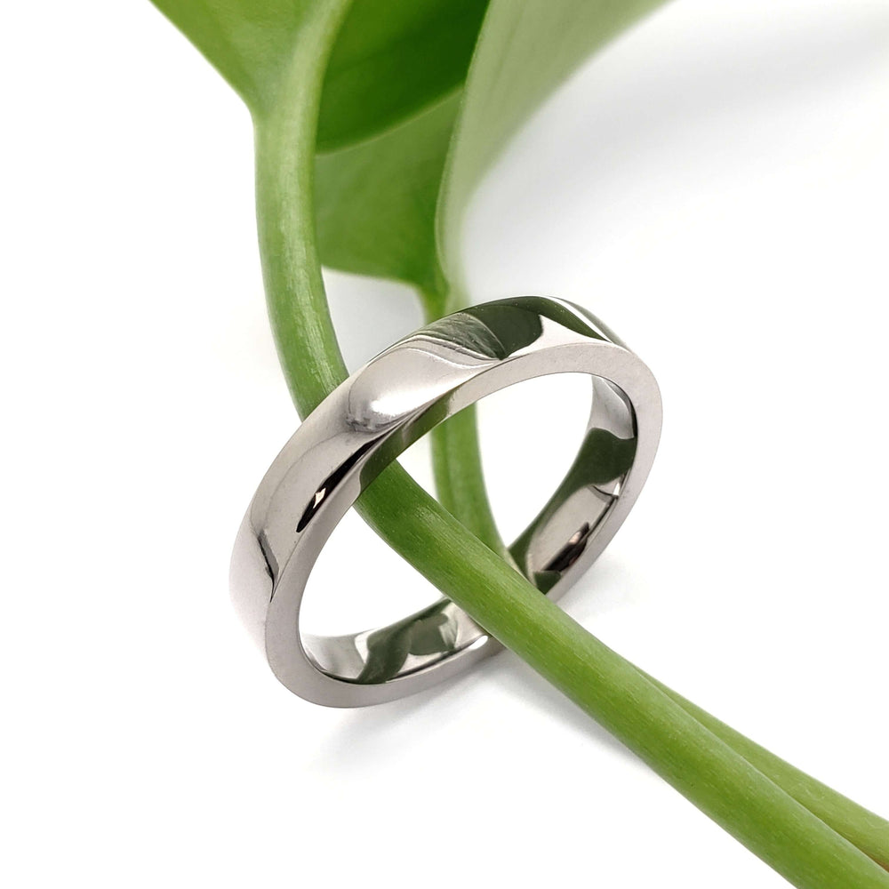 Handcrafted 14kt palladium white gold wedding ring displayed on green stem