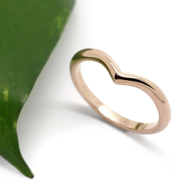 Handcrafted 14kt rose gold chevron wedding ring beside a green leaf