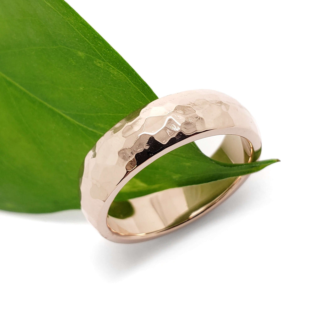 Handcrafted 14kt rose gold hammered wedding ring resting on a green leaf