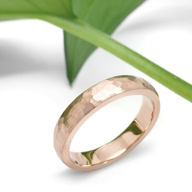 Handcrafted 14kt rose gold hammered wedding ring beside a green leaf