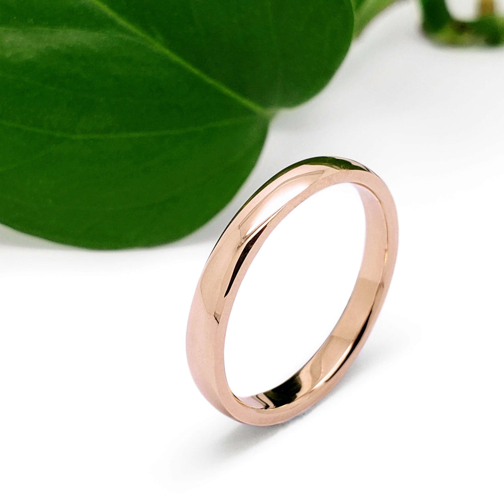 Handcrafted 14kt rose gold wedding ring with low dome profile, near green leaf