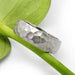 Handcrafted 14kt white gold hammered wedding ring resting on a green stem
