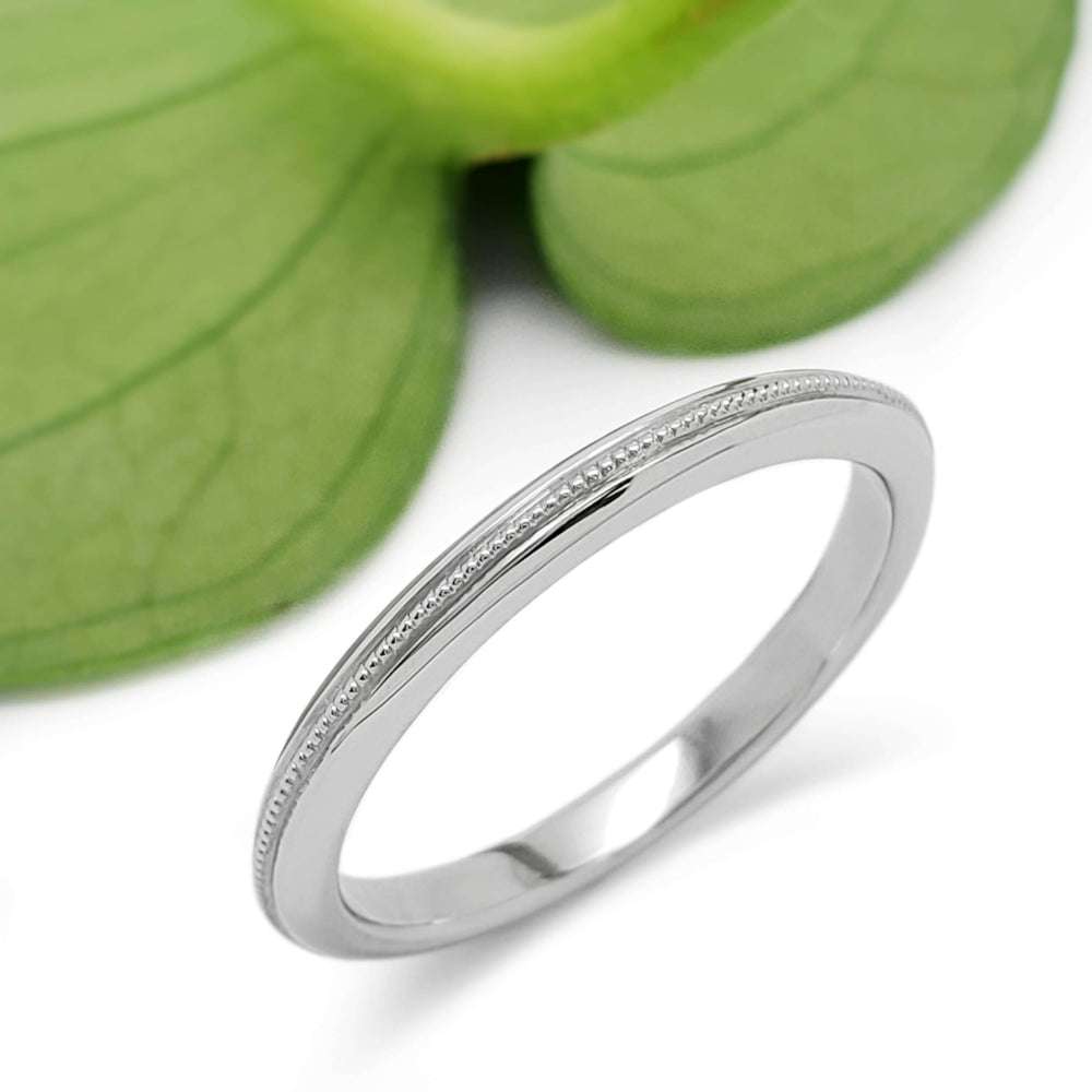 Handcrafted 14kt white gold millgrain wedding ring beside a green leaf