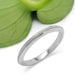 Handcrafted 14kt white gold millgrain wedding ring beside a green leaf