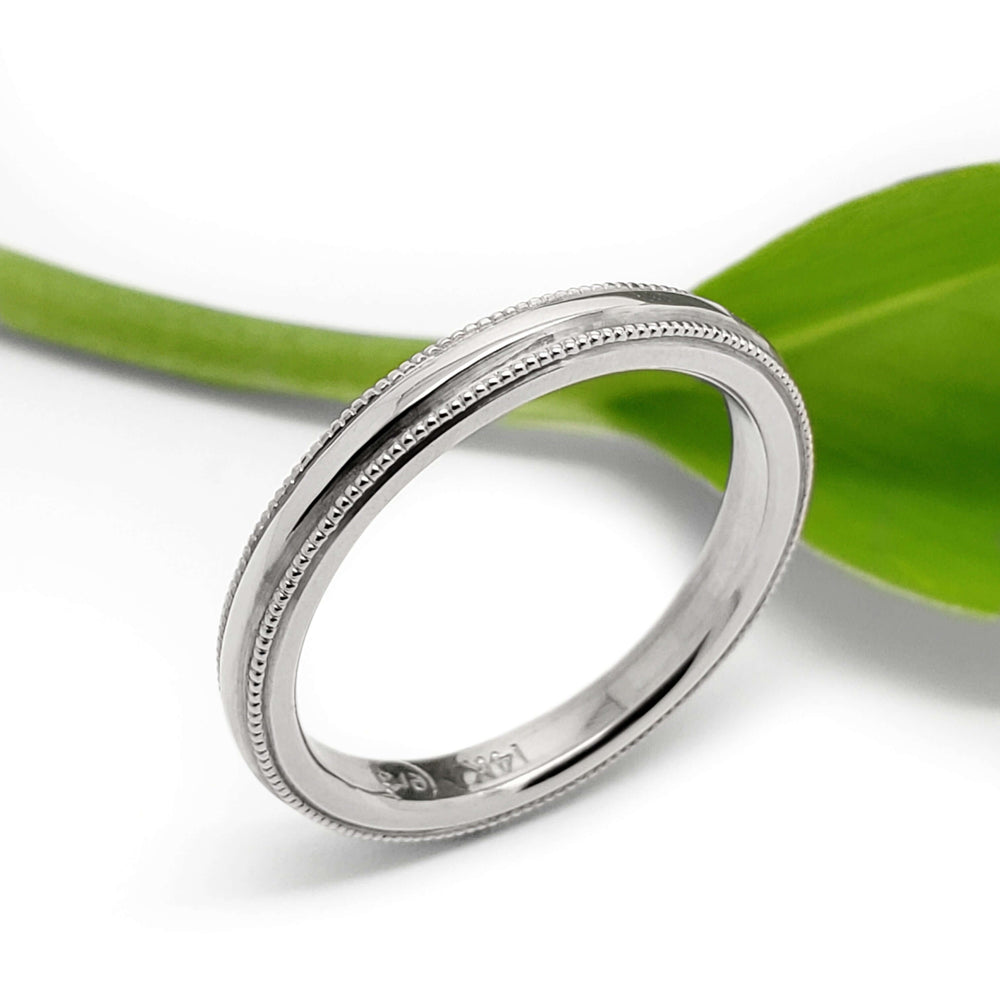Handcrafted 14kt white gold millgrain wedding ring beside a green leaf