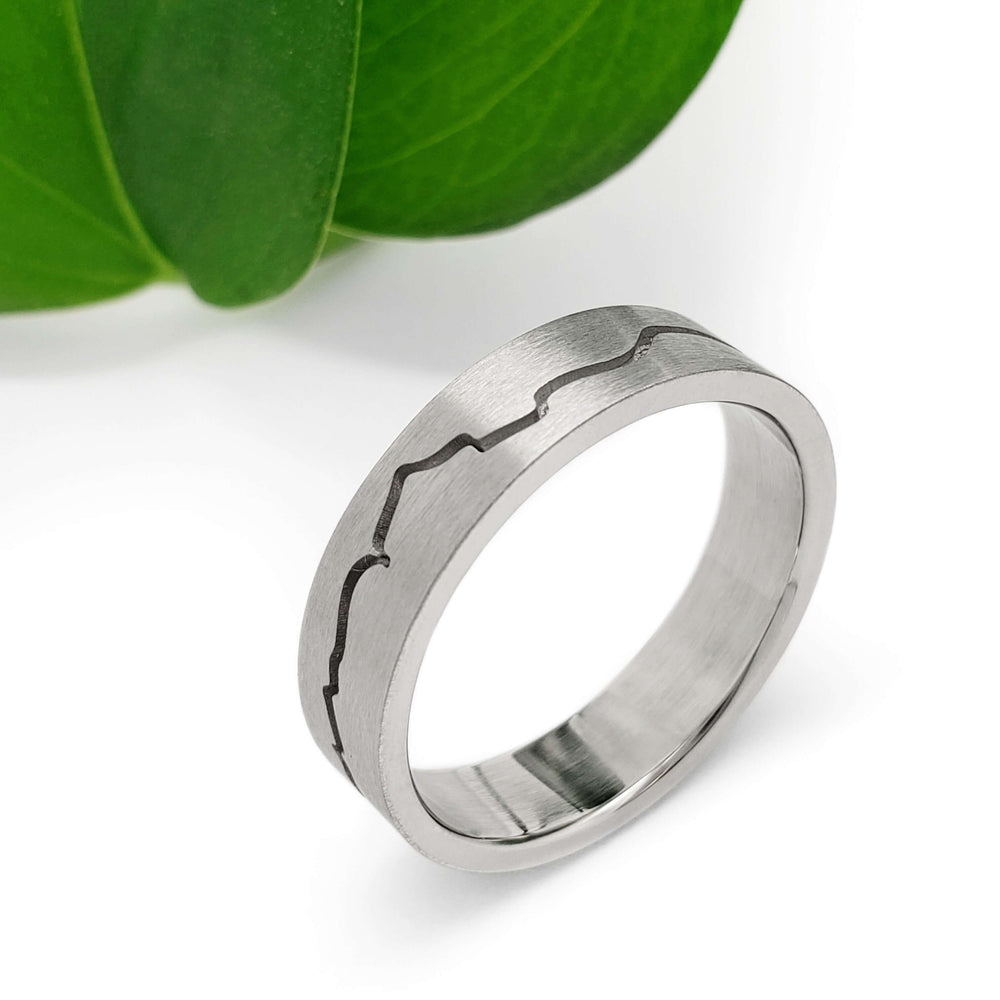 Handcrafted 14kt white gold mountain range ring with brushed texture, shown near a green leaf