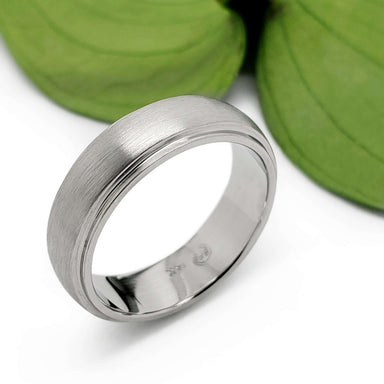 Handcrafted 14kt white gold wedding ring with brushed texture near green leaves