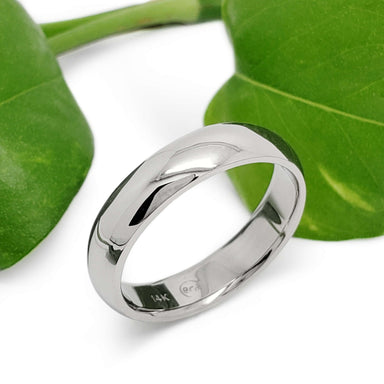 Handcrafted 14kt white gold wedding ring with high polish beside green leaves