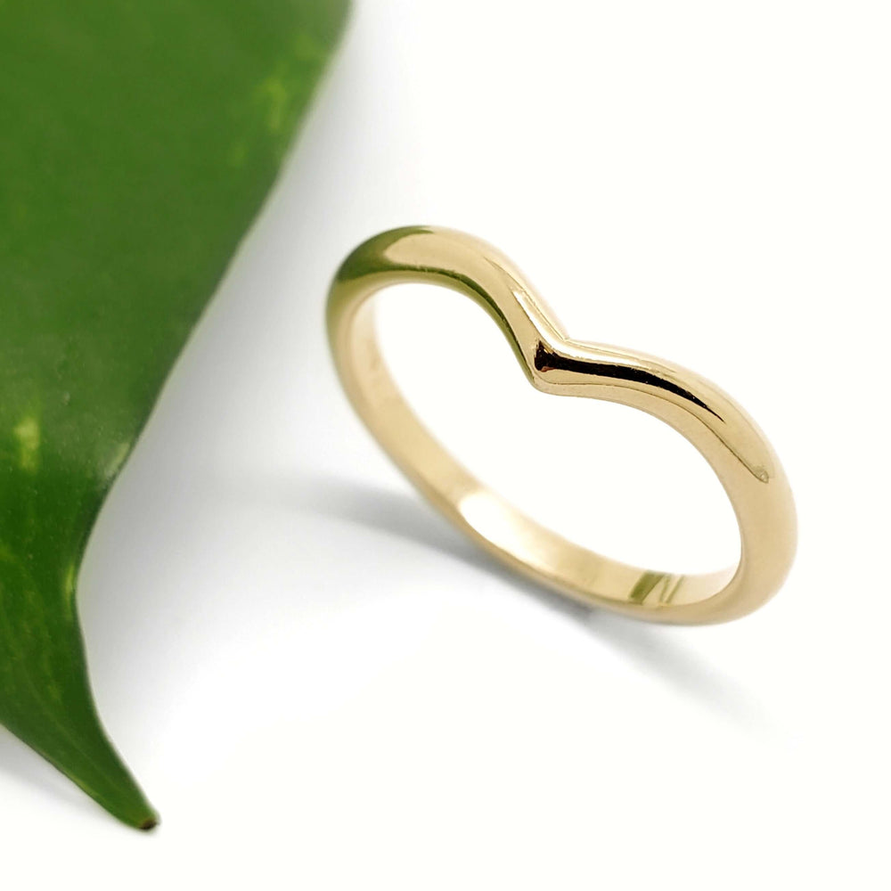 Handcrafted 14kt yellow gold chevron ring beside a green leaf