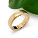 Handcrafted 14kt yellow gold wedding ring with millgrain detail beside a green leaf