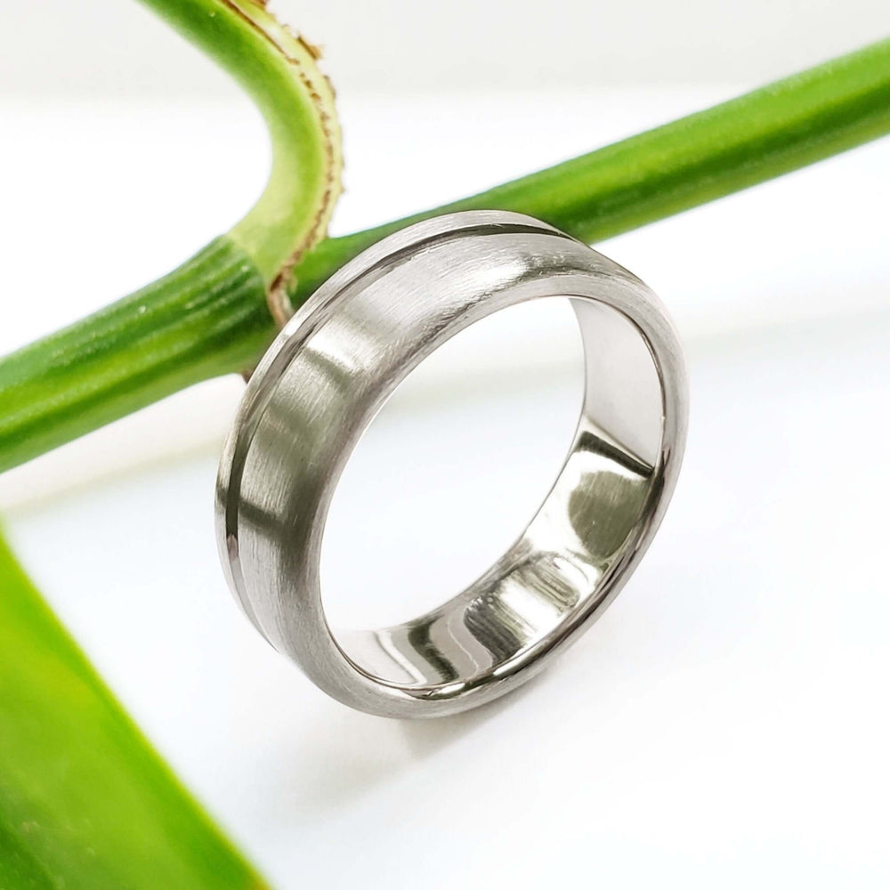 Handcrafted brushed 14kt white gold ring with carved wave detail, shown on plant stem